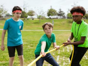 Group of kids playing tug of war in a sunny park, wearing colorful headbands.