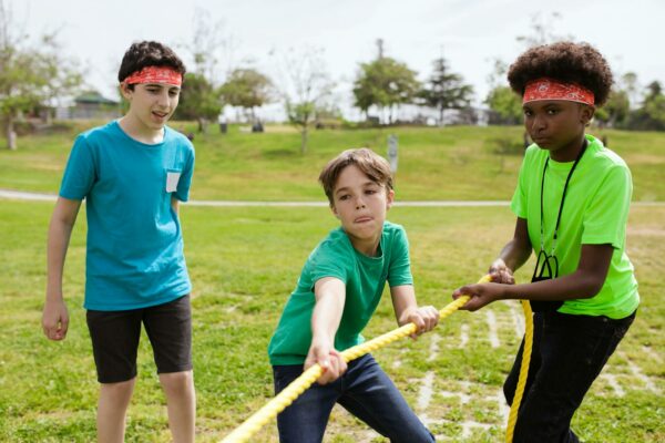 Group of kids playing tug of war in a sunny park, wearing colorful headbands.